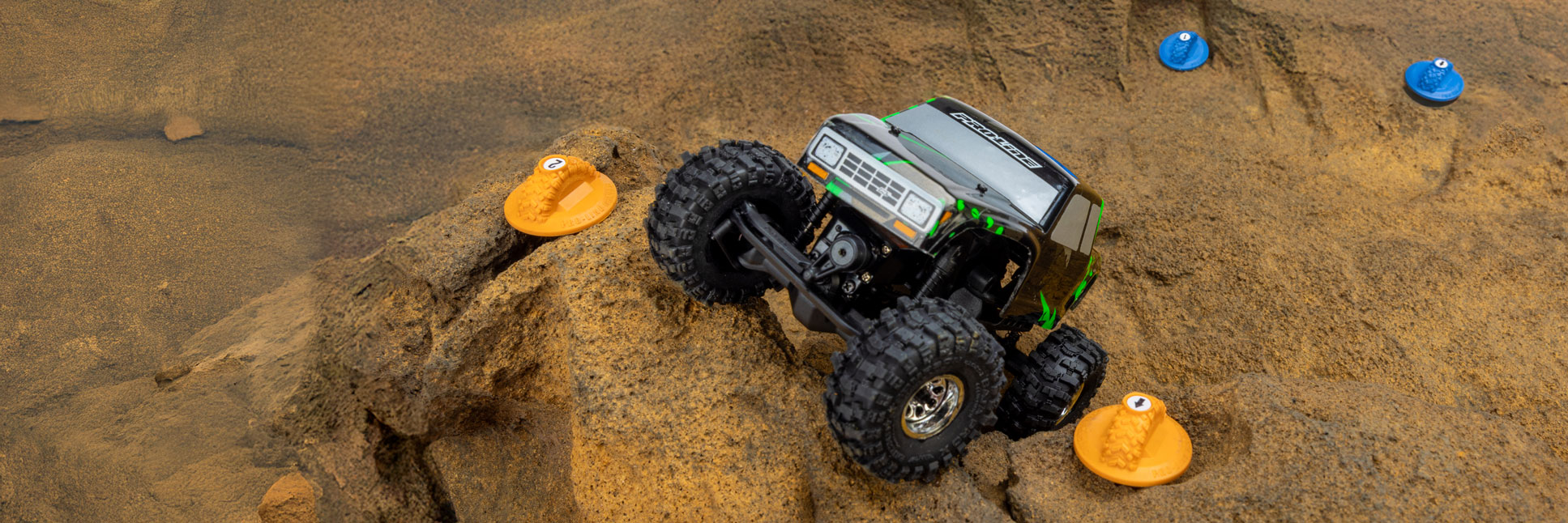 Action shot of the Pro-Line Blue and Orange Gate Marker Set used as a course route on a rocky surface to define direction for a RC rock crawler